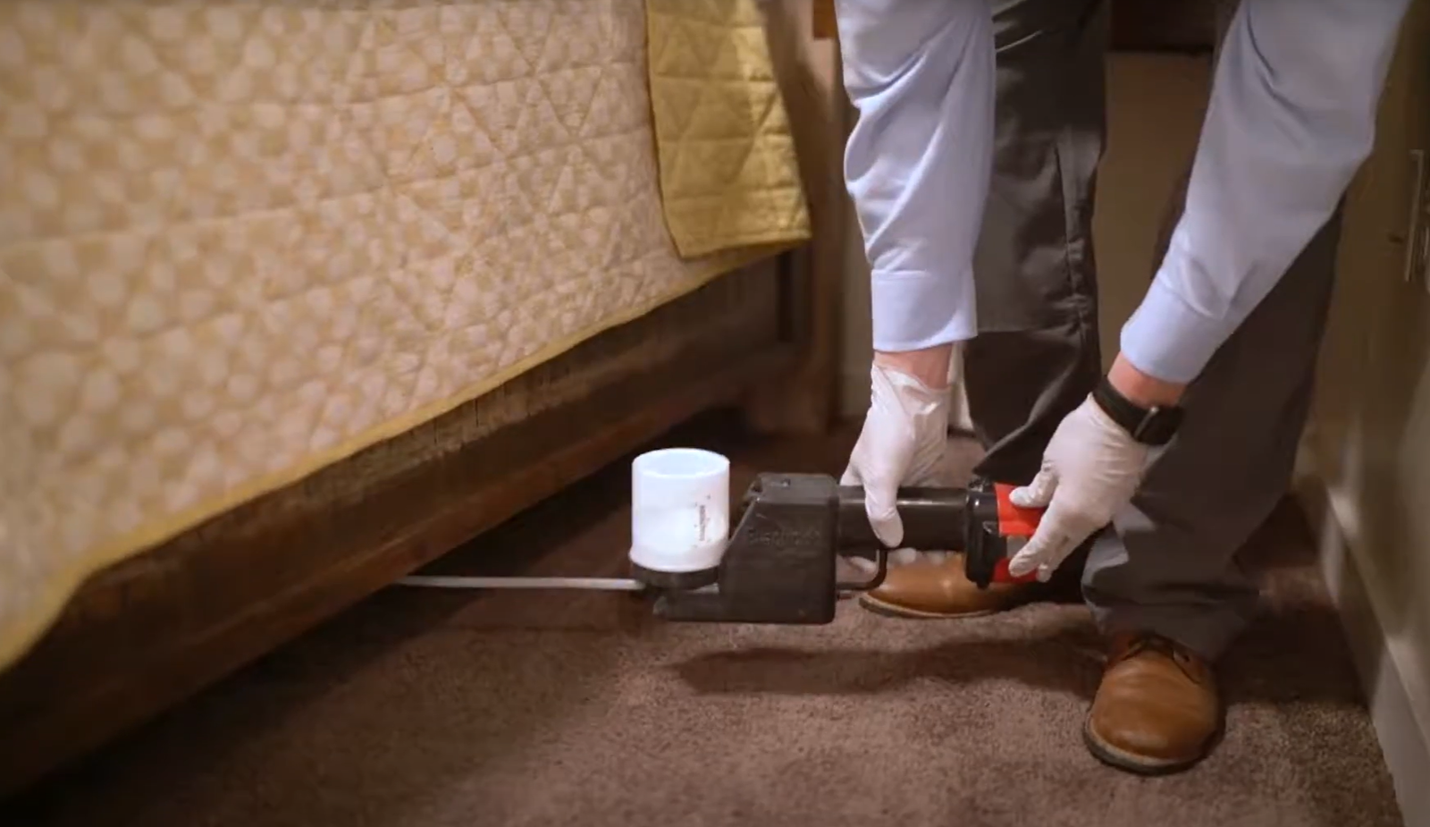 Professional applying pest control treatment under a bed frame, representing Pest Control Service in Cicero for indoor infestations.