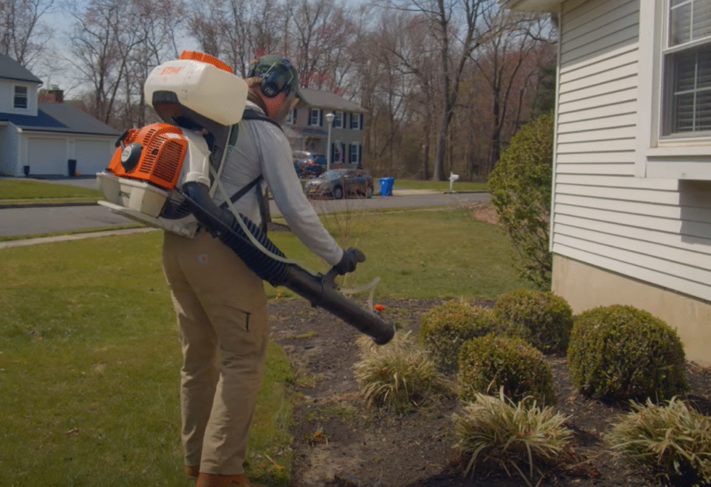Worker using a backpack sprayer to treat a home’s exterior and yard, showing Pest Control Service in Cicero for outdoor pest prevention.